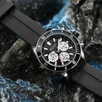 Luxury motorsport-inspired chronograph watch with black bezel and rubber strap on dark rocks