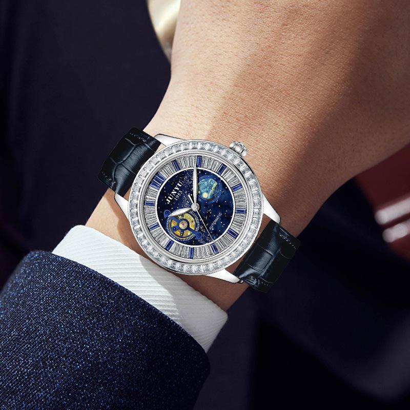 Luxury sport watch with blue galaxy dial, diamond bezel, and black leather strap on wrist