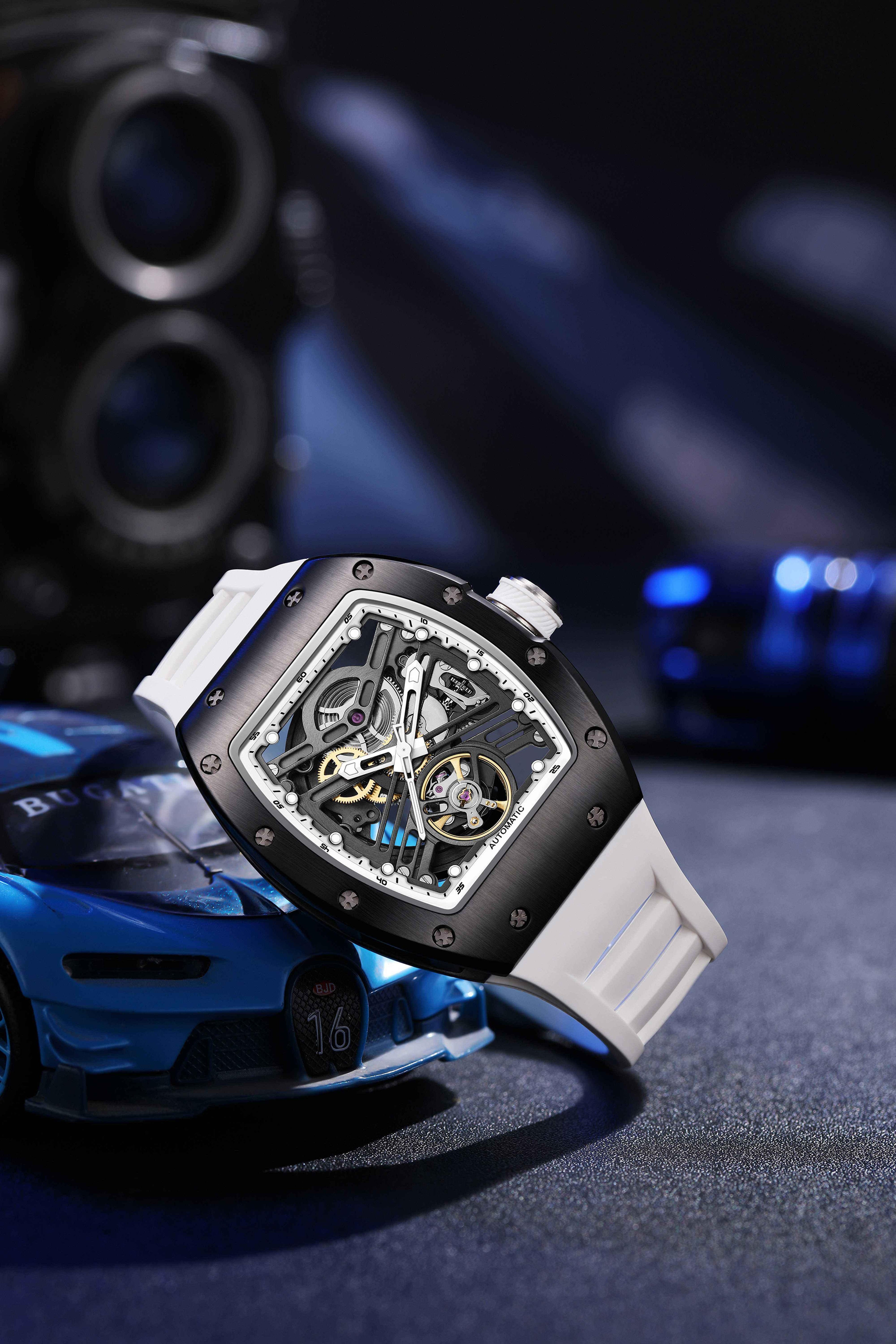 Motorsport-inspired skeleton automatic watch with tonneau case and white strap, sporty car backdrop
